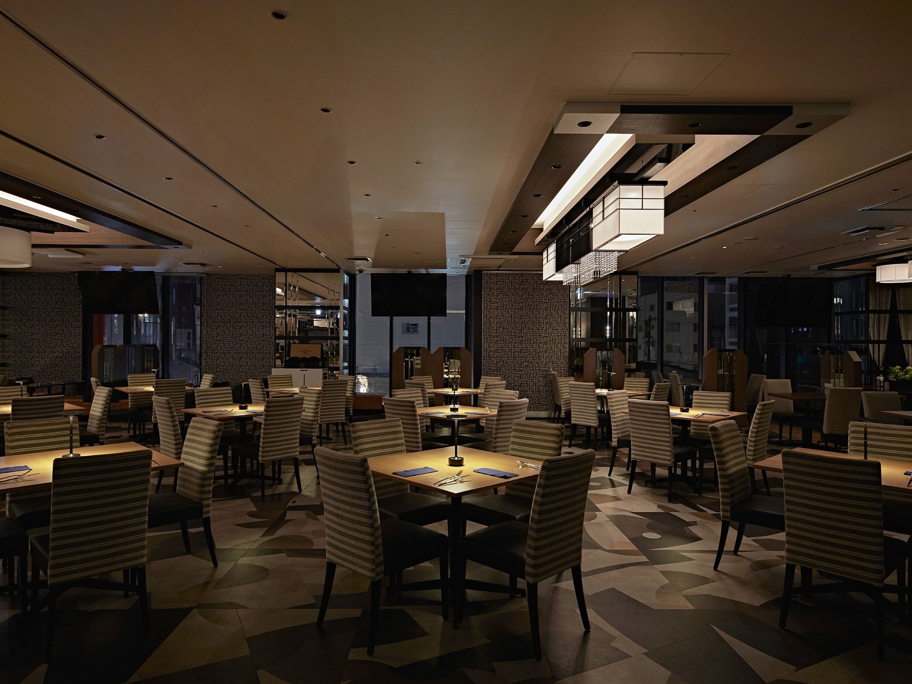 Un restaurante moderno con un patrón geométrico en el suelo, sillas a rayas e iluminación contemporánea.