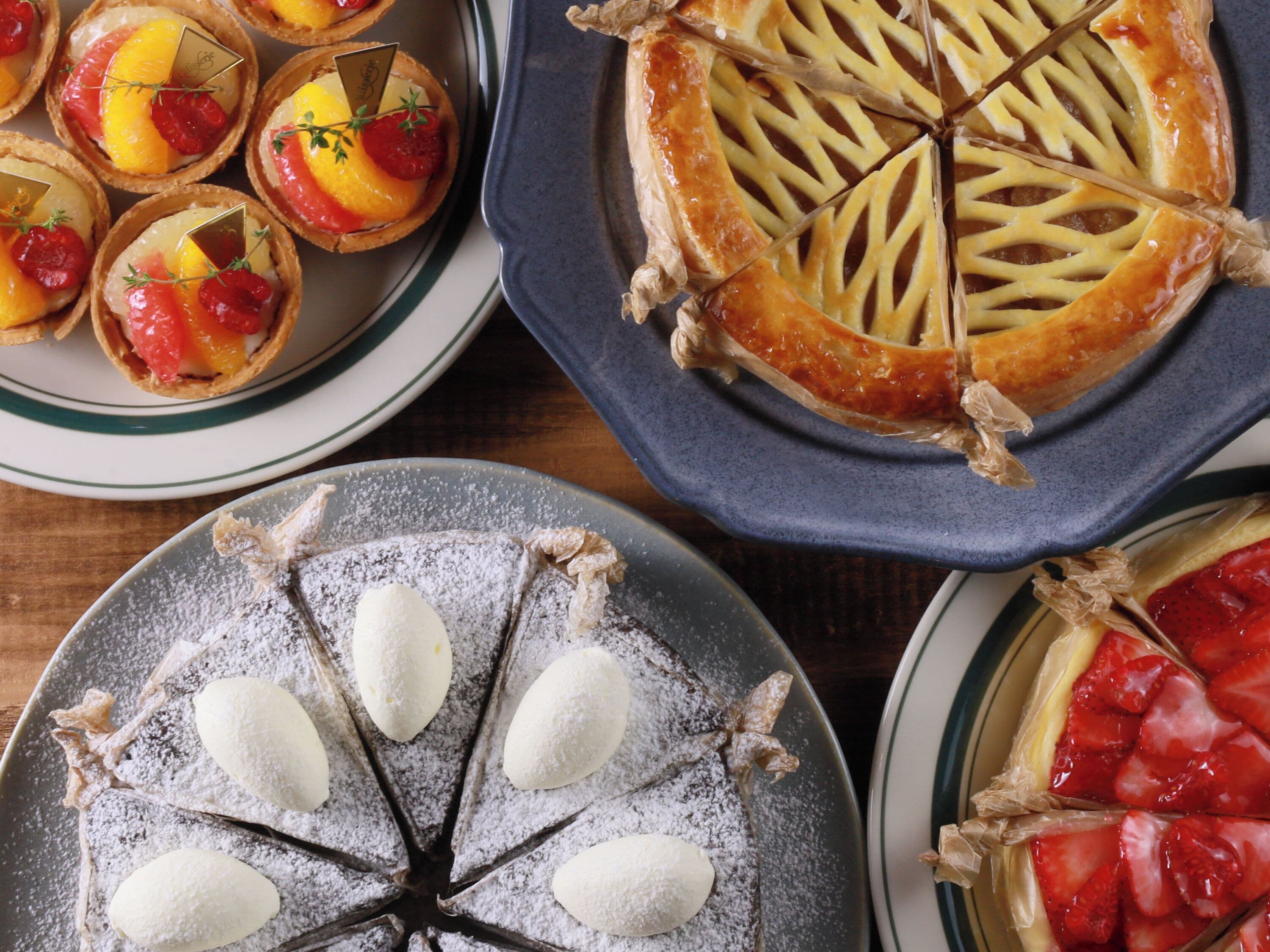 A variety of desserts including tarts, a pie, and a cake with powdered sugar and almonds.