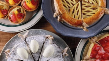 A variety of desserts including tarts, a pie, and a cake with powdered sugar and almonds.
