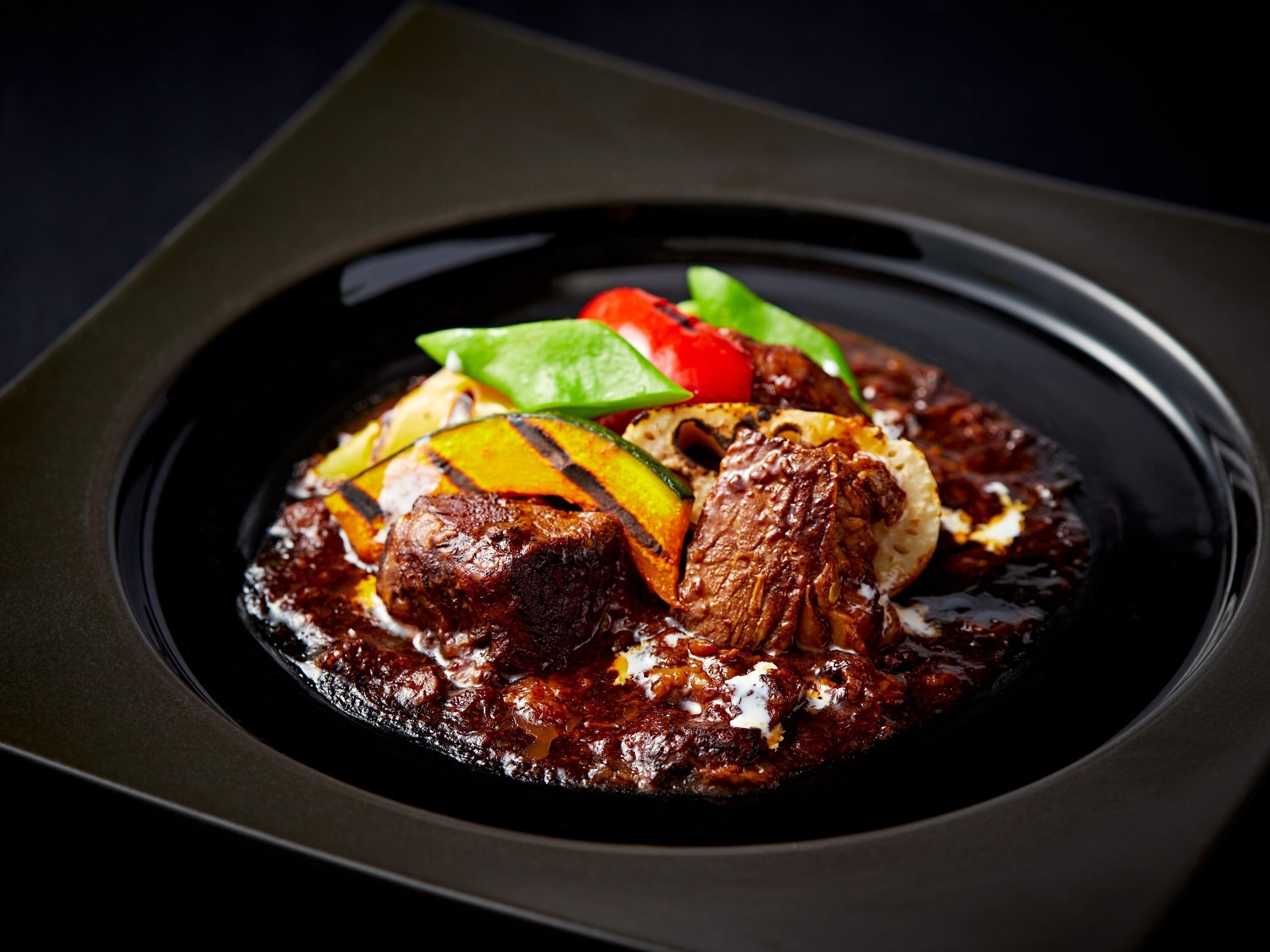 A dish with grilled vegetables and meat on a black plate.