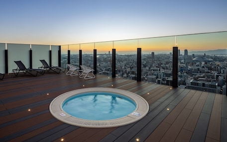 A rooftop terrace with a hot tub, lounge chairs, and a city view.