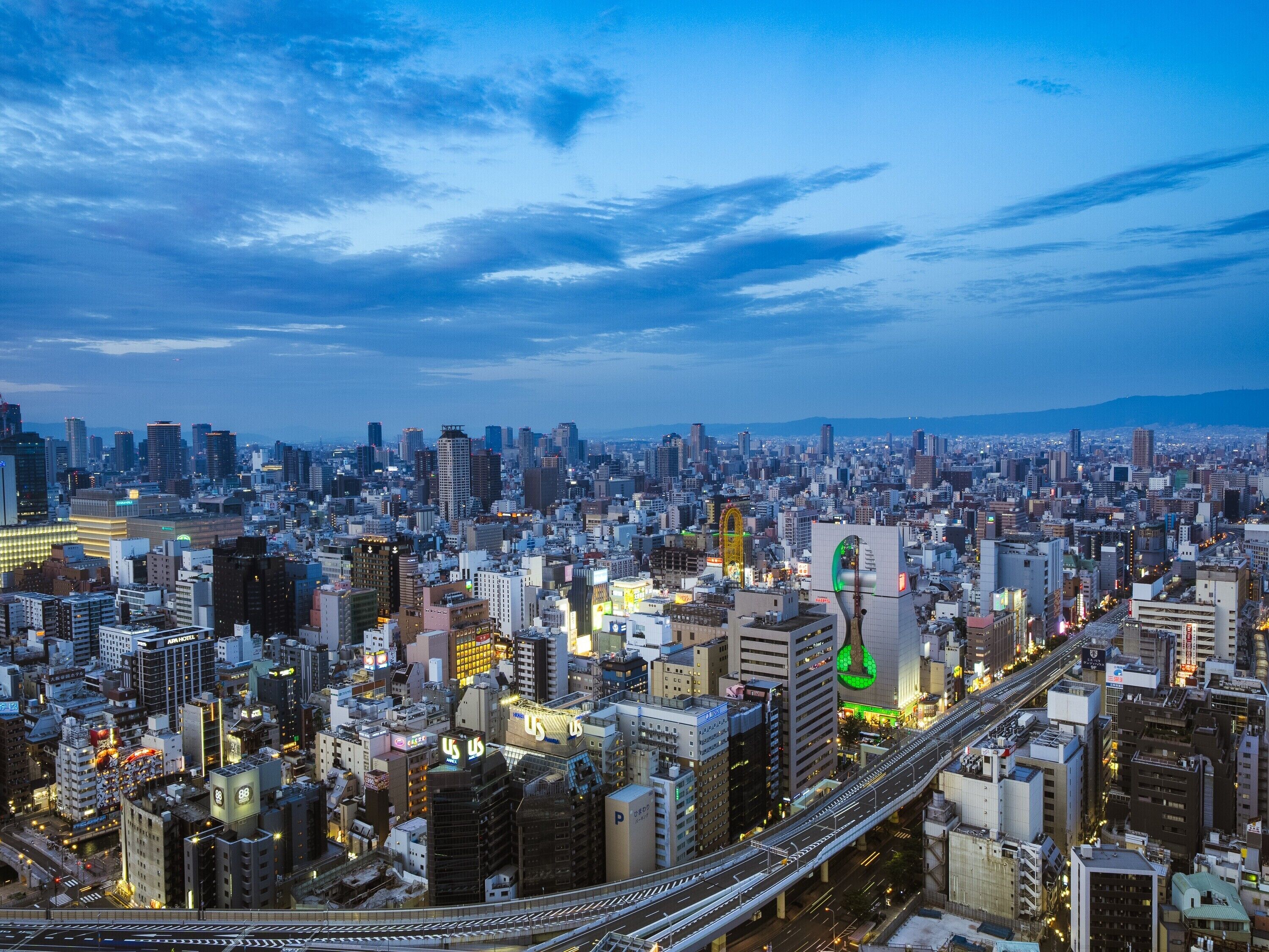A cityscape at dusk with a prominent building featuring a green circular logo.