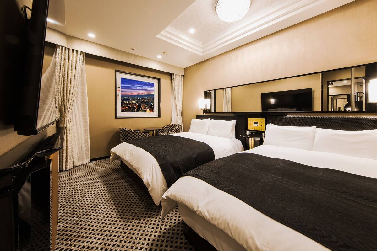 Een hotelkamer met twee bedden, een televisie, een bureau en uitzicht op de stad.