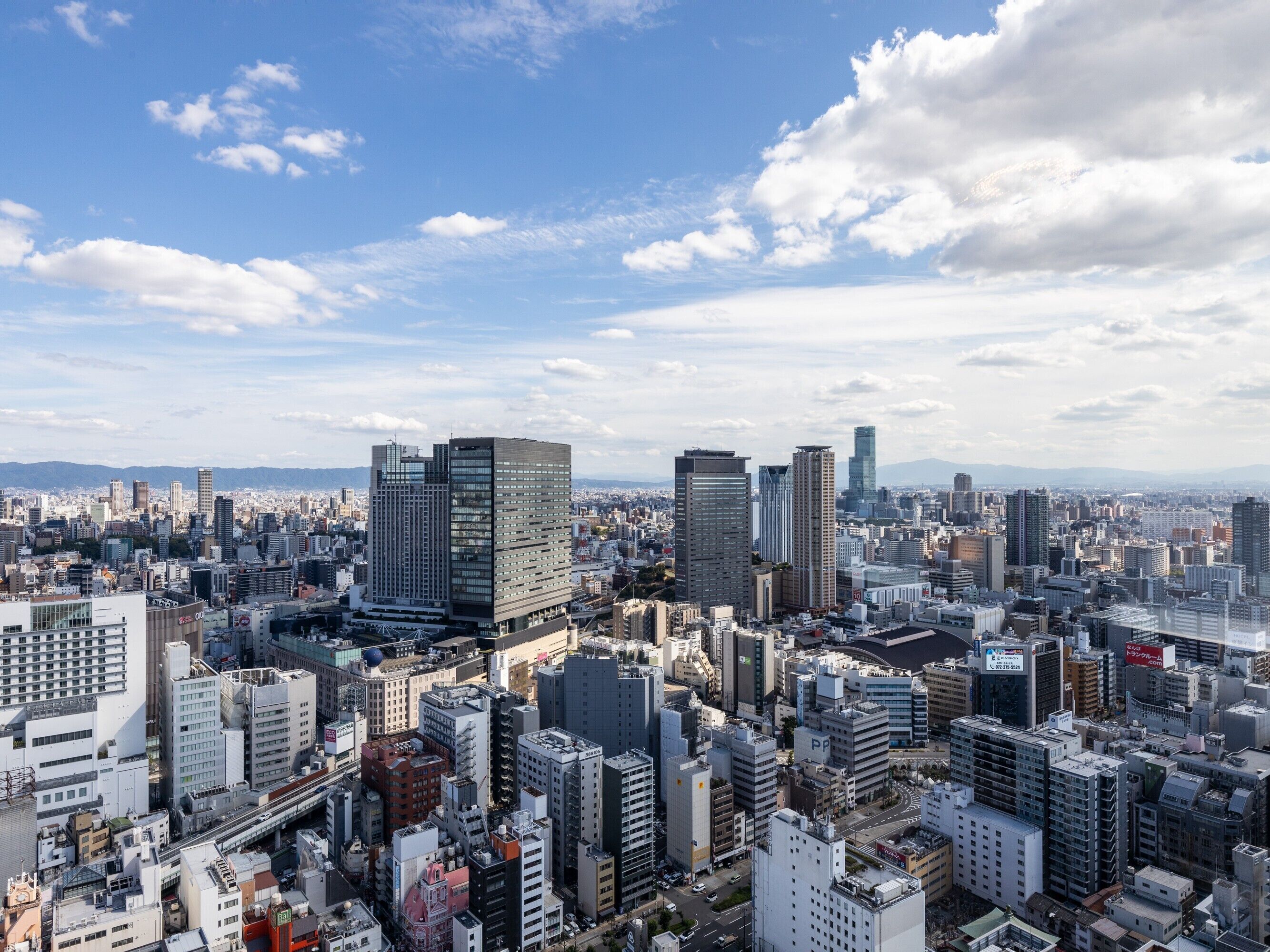 A cityscape with various buildings, including high-rise structures and smaller buildings, under a partly cloudy sky.