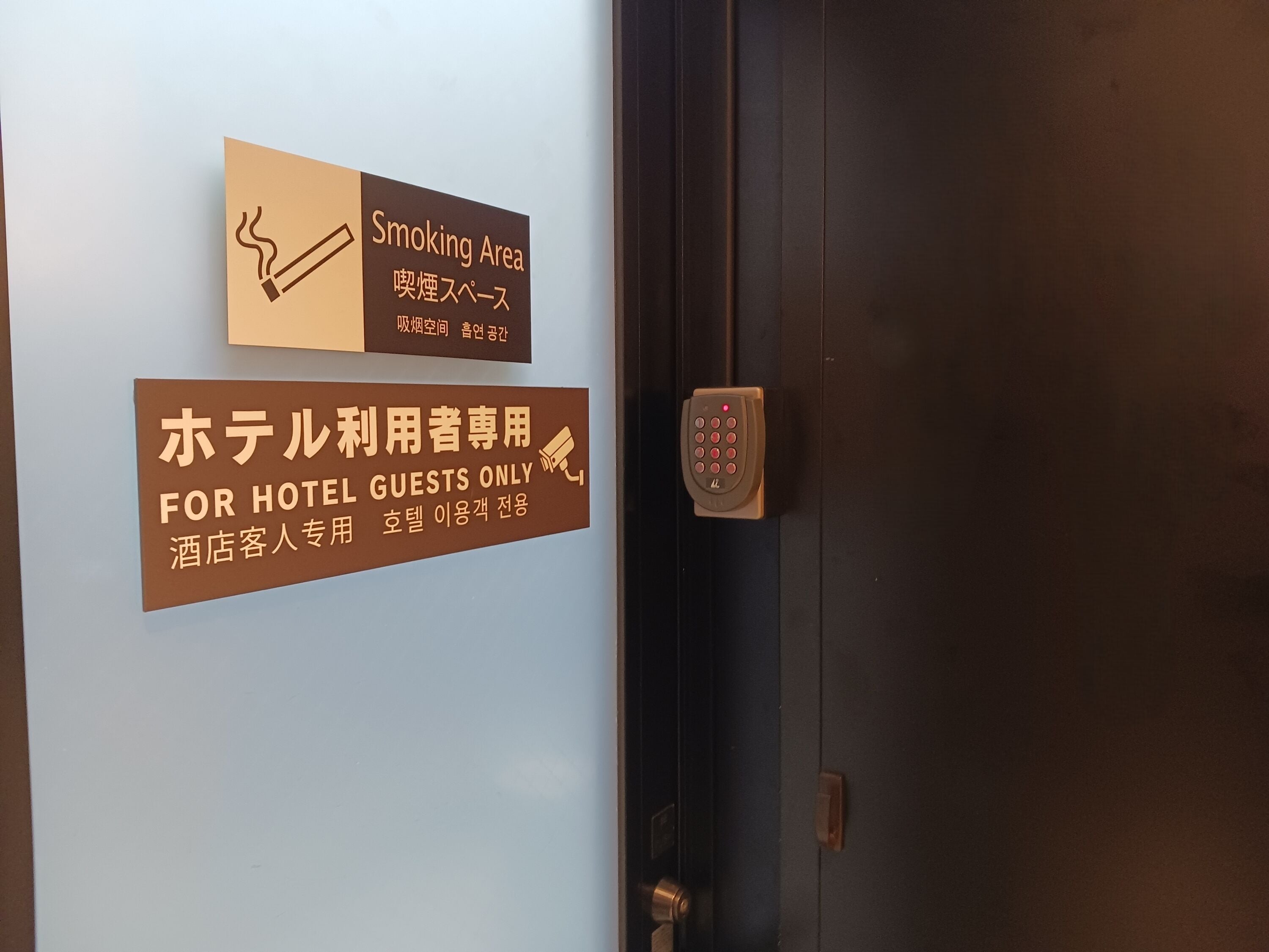 A door with a sign indicating a smoking area and a sign for hotel guests only.