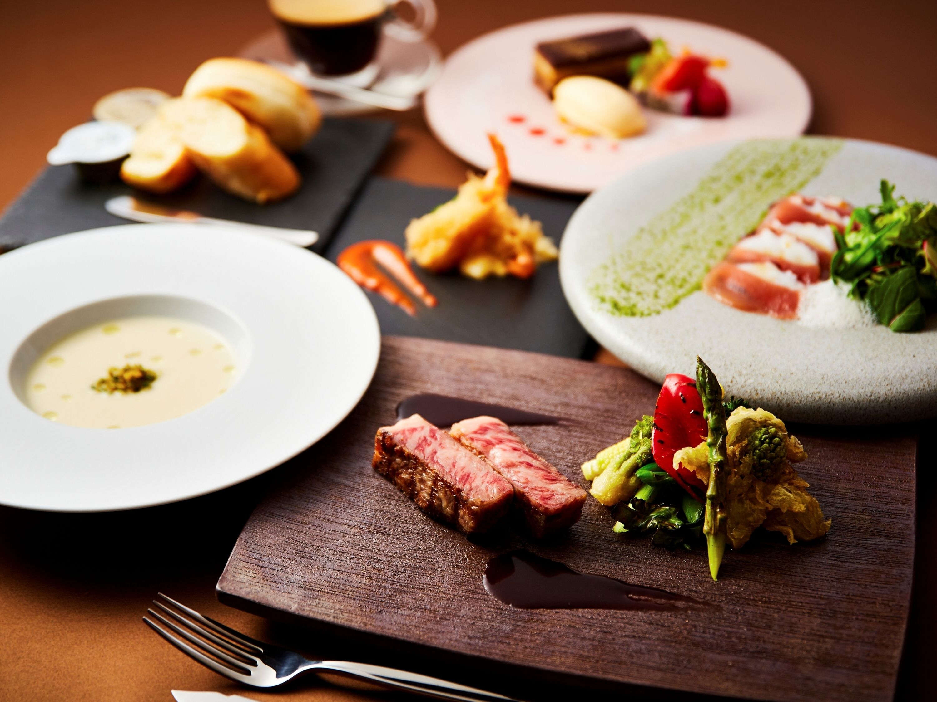 A variety of dishes on a wooden table, including a plate with a green sauce, a plate with a white sauce, and a plate with a red sauce.