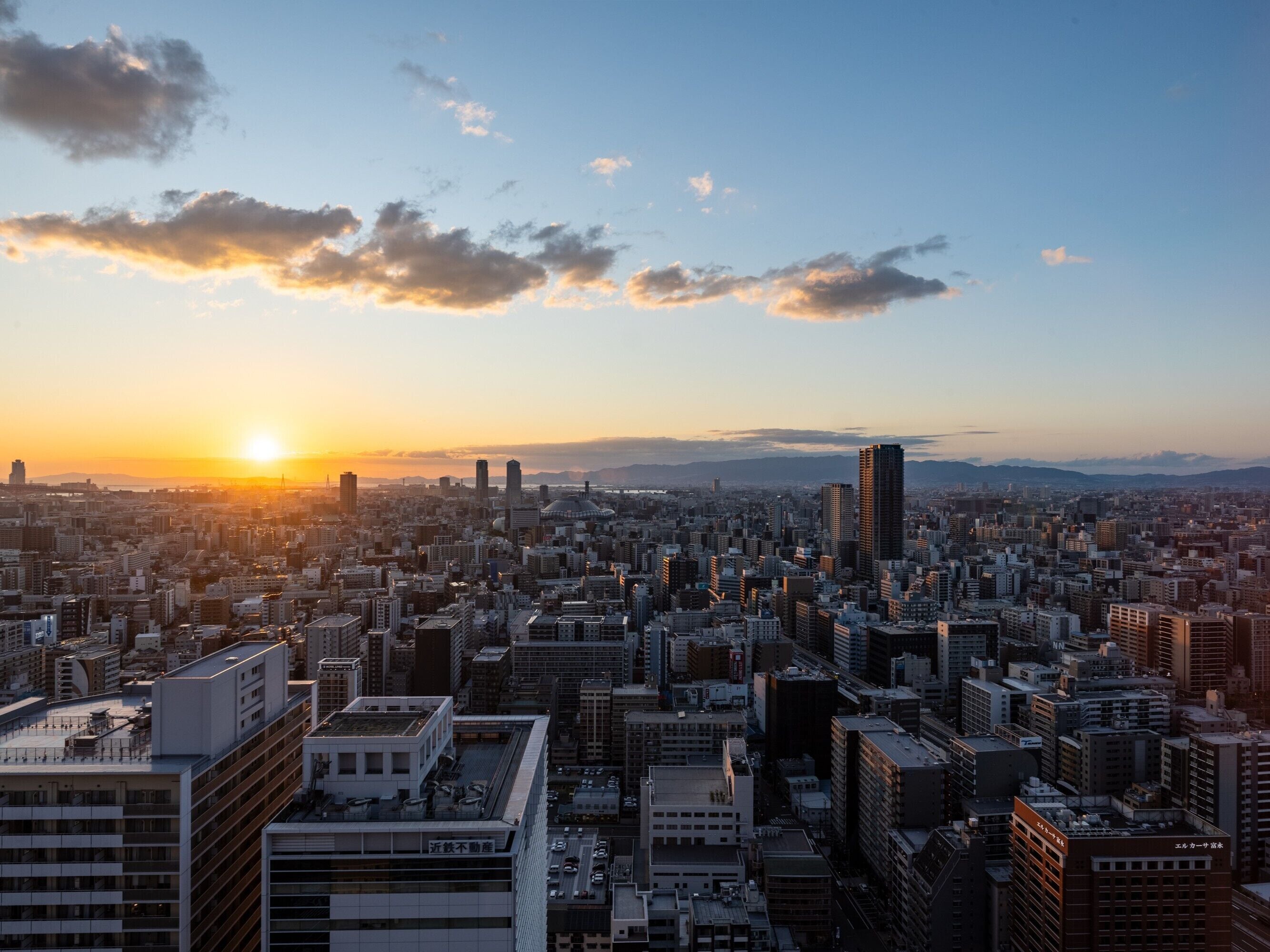 A cityscape at sunset with a variety of buildings, including high-rise structures and smaller residential buildings.