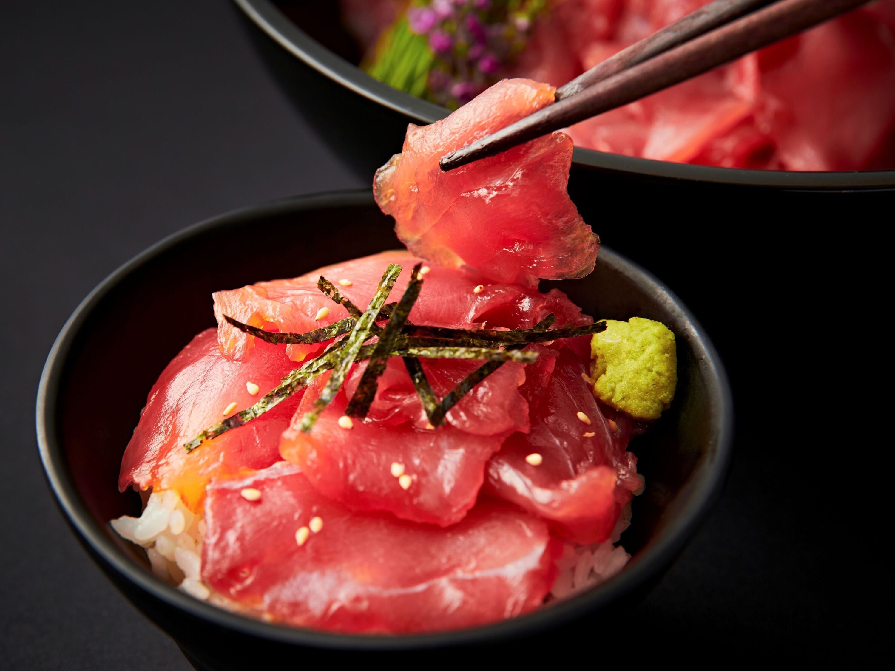 A bowl of sashimi with rice and garnishes.