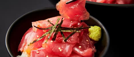 A bowl of sashimi with rice and garnishes.