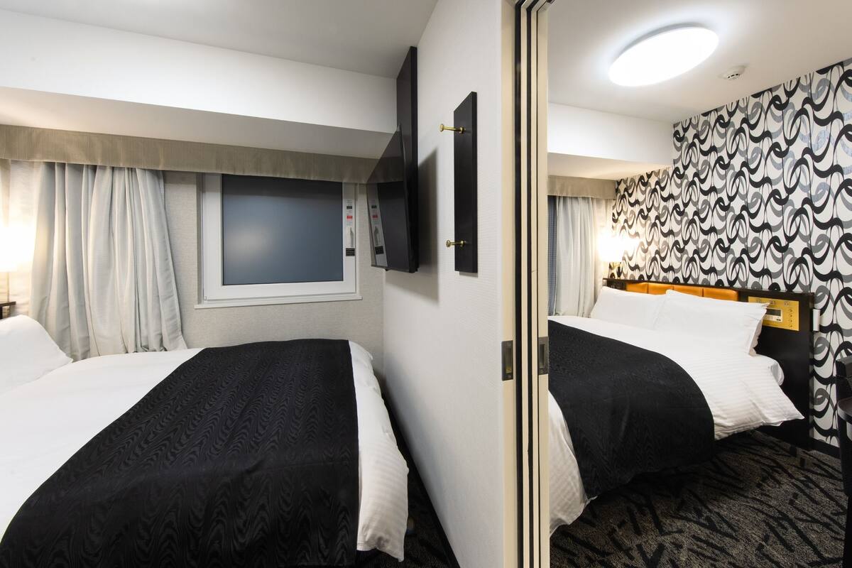 Hotelkamer met twee bedden, een televisie, een raam met gordijnen, een behangen muur en een vloerbedekking.