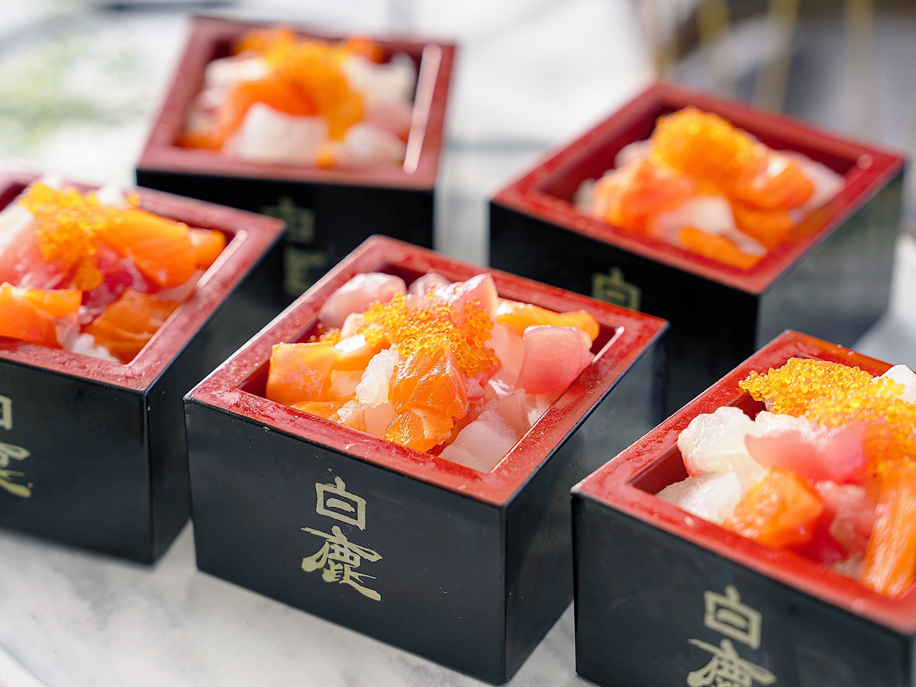 A series of square containers with a red rim, each containing a mix of diced fruit and a white substance, possibly a dessert or condiment.