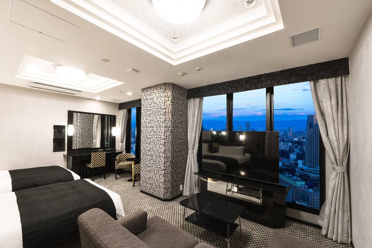 Een moderne hotelkamer met een groot bed, een bank, een televisie en uitzicht over de stad.