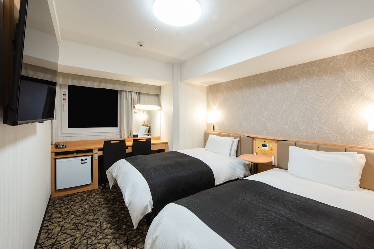 Een hotelkamer met twee bedden, een bureau, een televisie en een minibar.