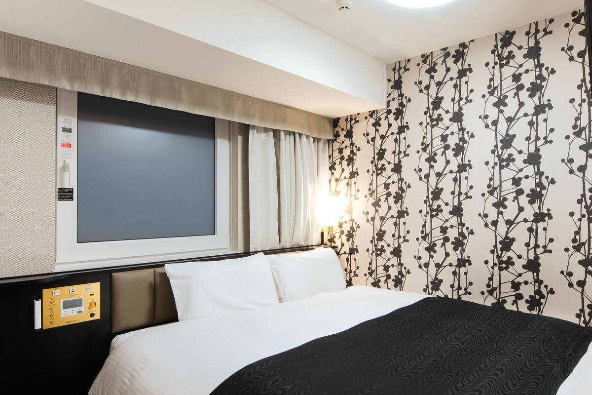 Een hotelkamer met een groot bed, een bedieningspaneel en een raam met gordijnen.