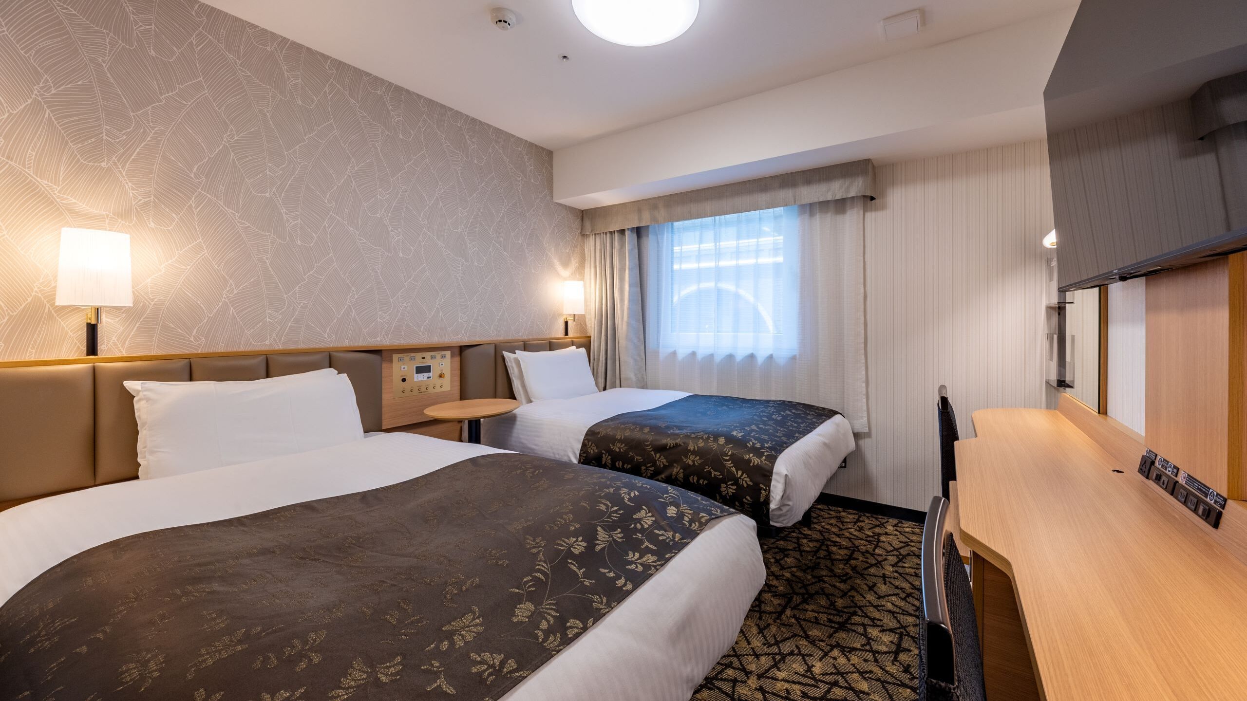 Une chambre d’hôtel avec deux lits, un bureau, une table de chevet, une lampe et une fenêtre avec des rideaux.