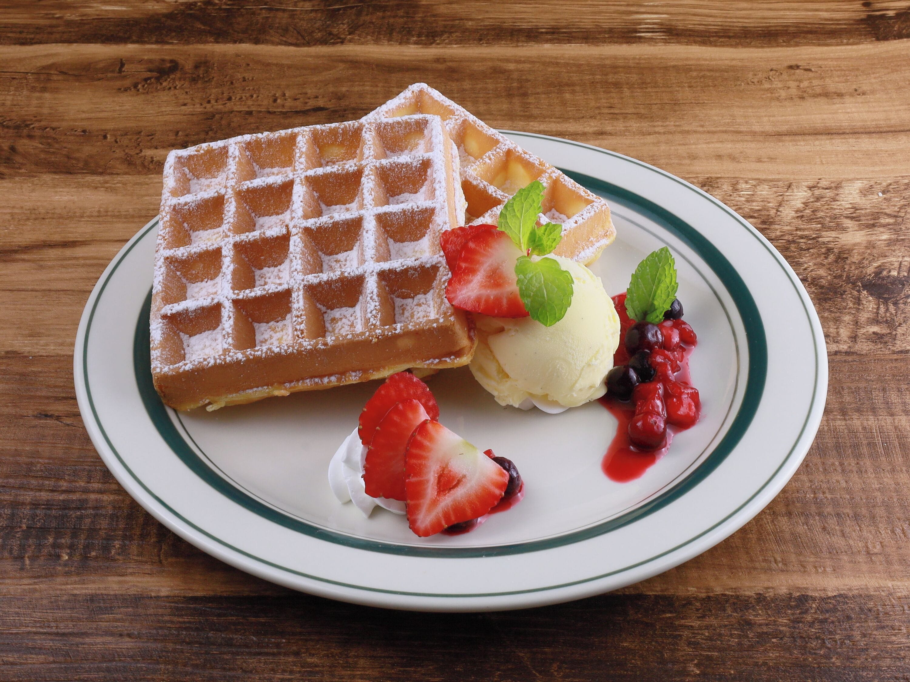 Une assiette avec un gaufre, une boule de glace à la vanille, des fraises et une sauce aux fruits rouges.