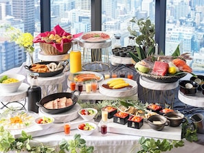 A buffet table with various food items and condiments, set against a cityscape view.