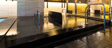 A modern indoor pool area with a wooden ceiling, a sign indicating a sleeping bath, and a glass partition.