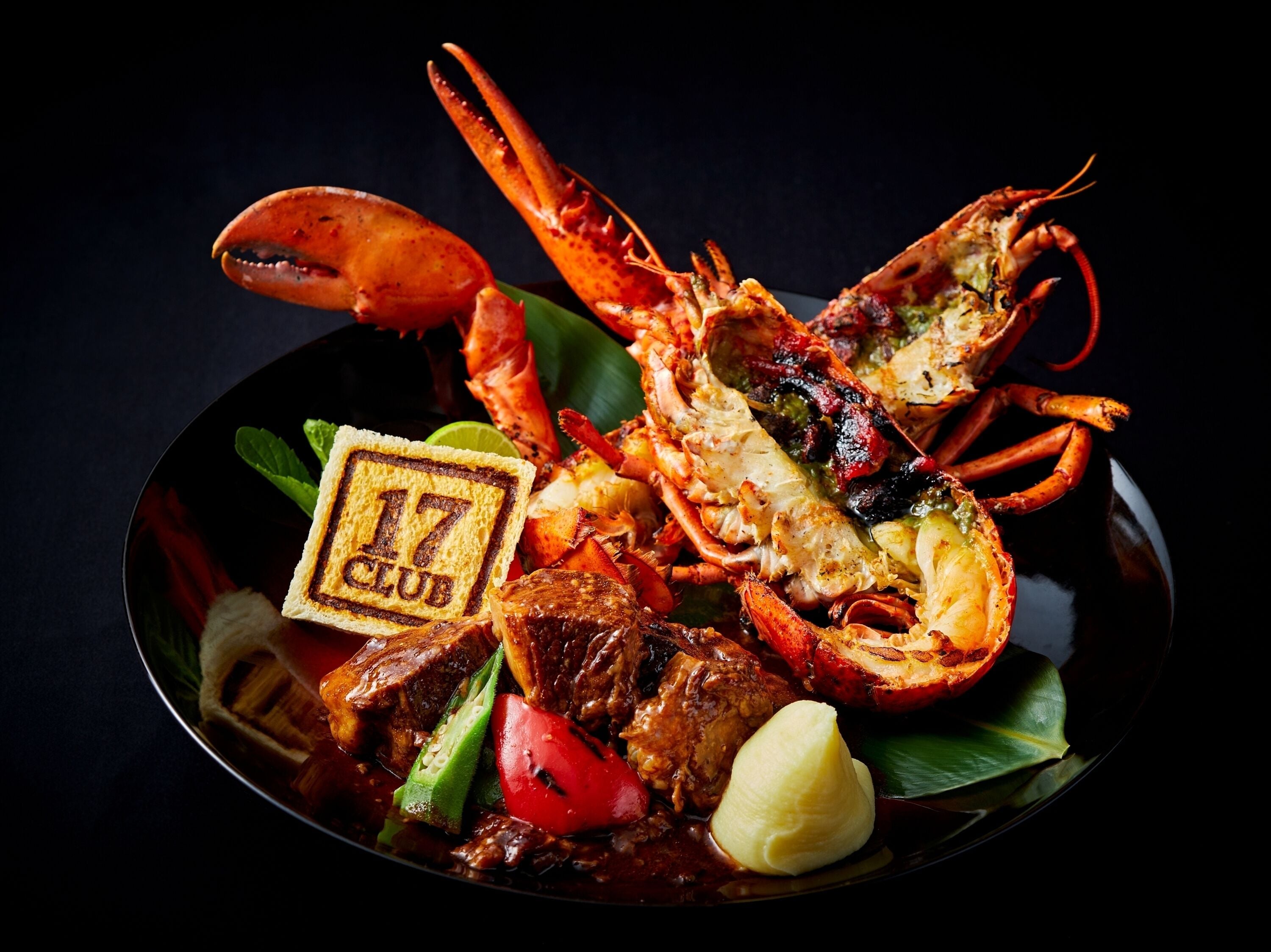 Una bandeja de mariscos con langosta, carne y vegetales sobre un plato oscuro.