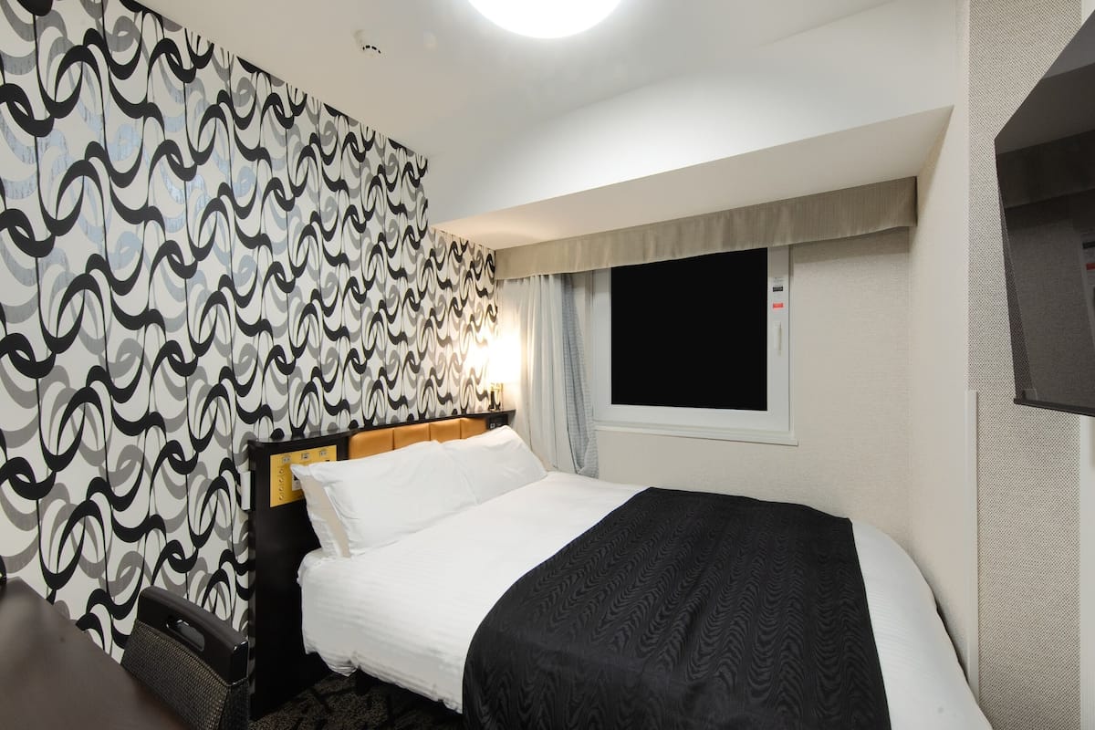 Een hotelkamer met een bed, een raam, een behang met patroon en een plafondlamp.