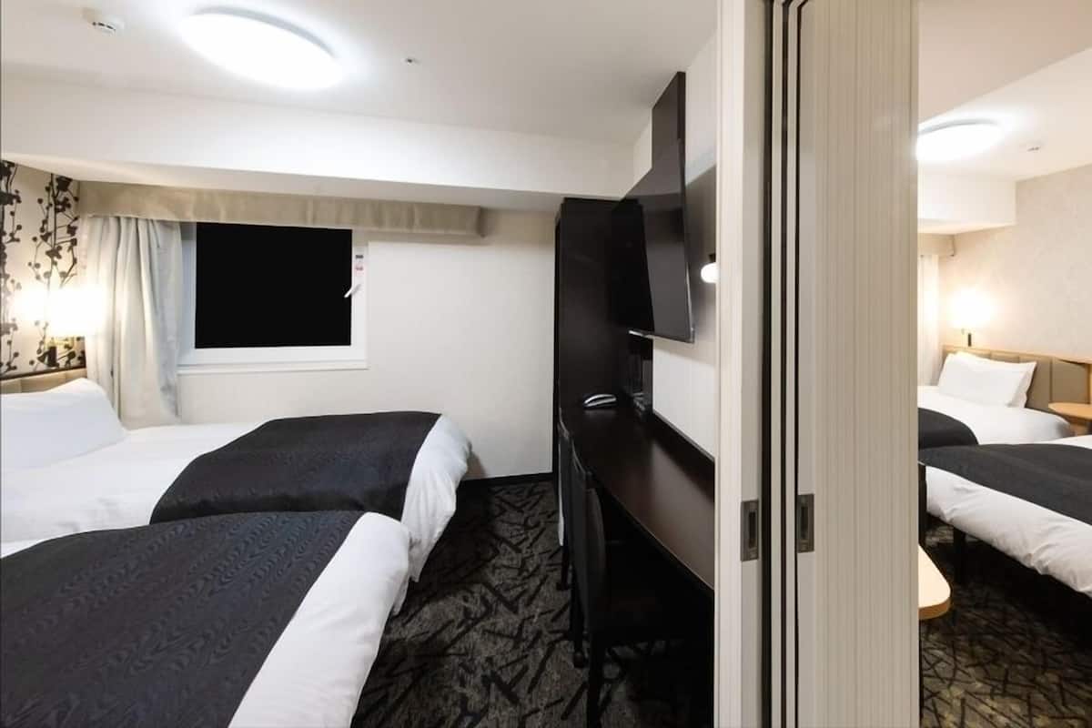 Een hotelkamer met twee bedden, een televisie, een raam met gordijnen en een nachtkastje met een lamp.