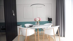 A modern dining area with a round table, white chairs, a vase with flowers, and a black lamp. - Phaedra's Studios in Kolymbari (Platanias)