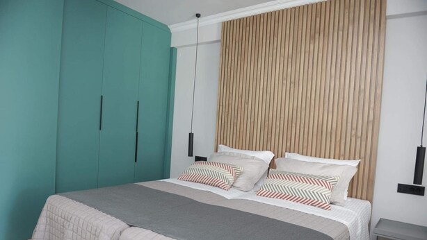A bedroom with a bed, a teal wardrobe, a wooden headboard, and a bedside table. - Phaedra's Studios in Kolymbari (Platanias)