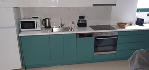 A modern kitchen with teal cabinets, a microwave, a kettle, a toaster, and an oven. - Phaedra's Studios in Kolymbari (Platanias)
