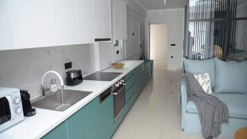 Una cocina moderna con armarios blancos, horno empotrado y una isla grande con un cuenco. En la sala de estar, hay un sofá azul claro con una manta y almohadas.