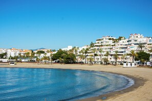 Un hotel frente al mar con varios pisos, palmeras y una playa al frente.