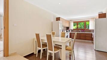 Una cocina moderna con armarios de madera, una mesa de comedor con sillas y vistas a zonas verdes por la ventana.