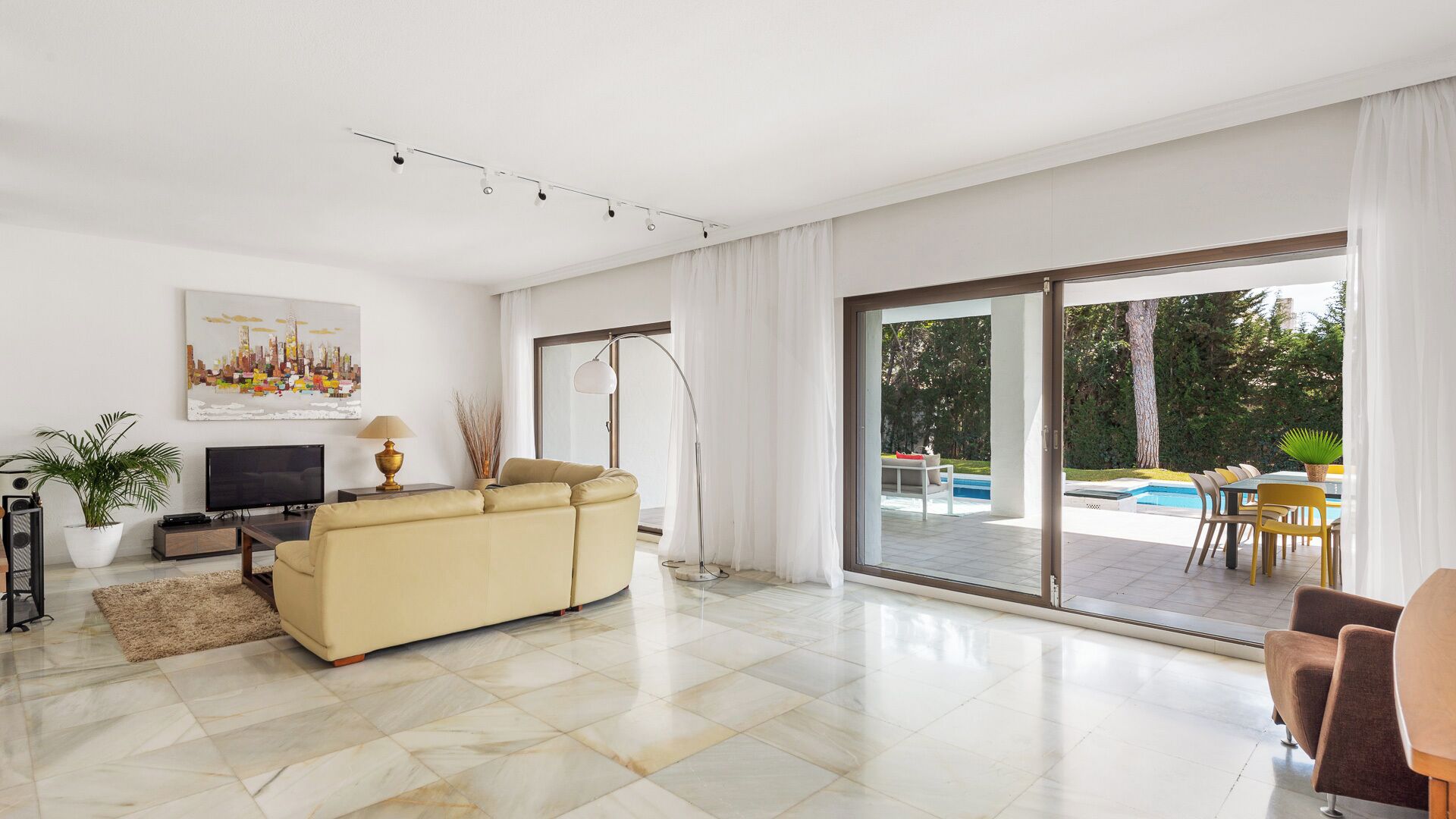 A spacious living room with a beige sofa, a flat-screen TV, and a painting on the wall.