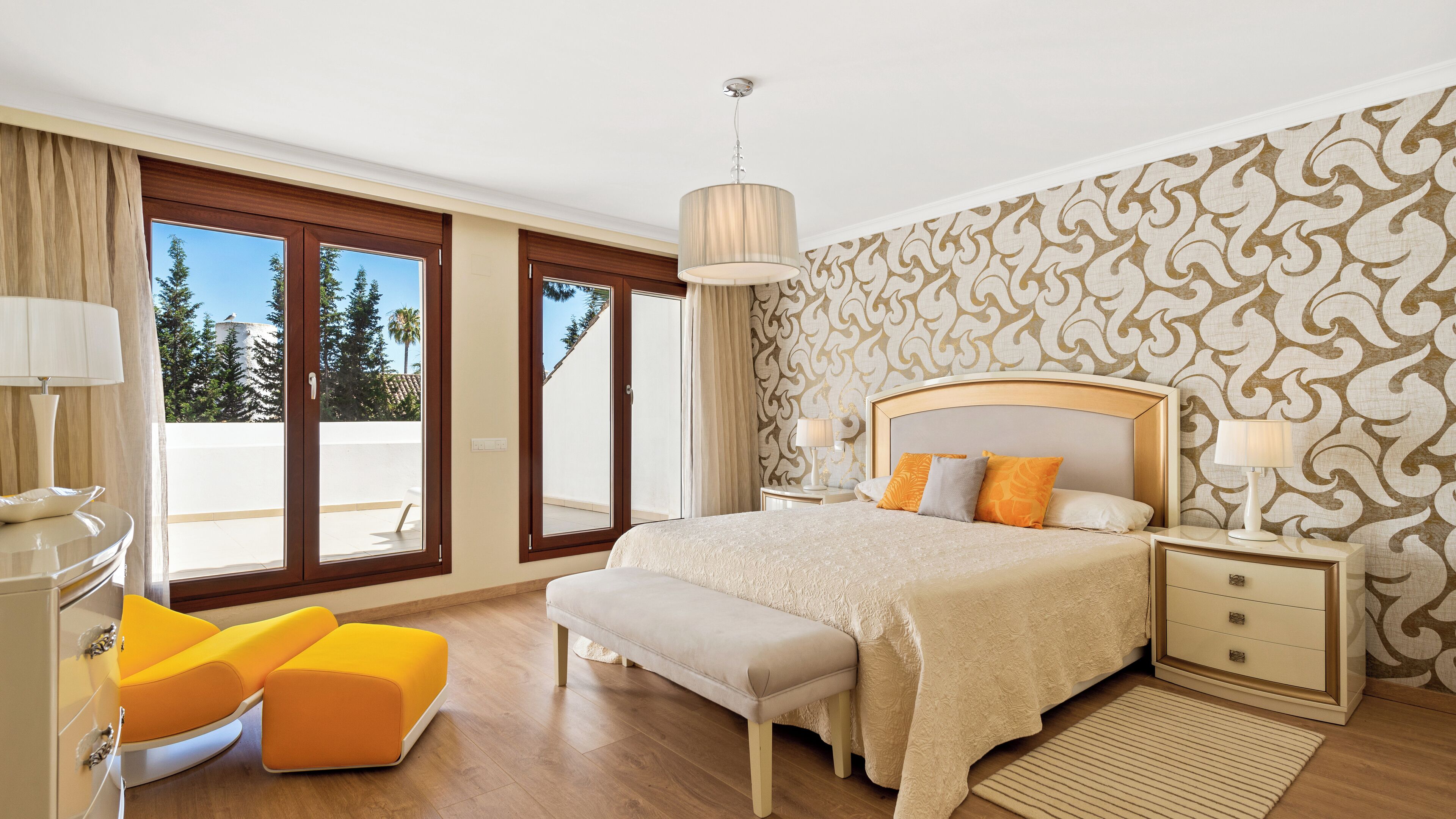 A bedroom with a large bed, a bench, a nightstand, and a view of the outdoors.