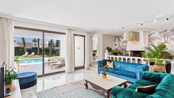 Un salon spacieux doté d’une grande porte-fenêtre coulissante donnant sur une piscine, d’un canapé bleu, d’un canapé vert et d’une table basse.