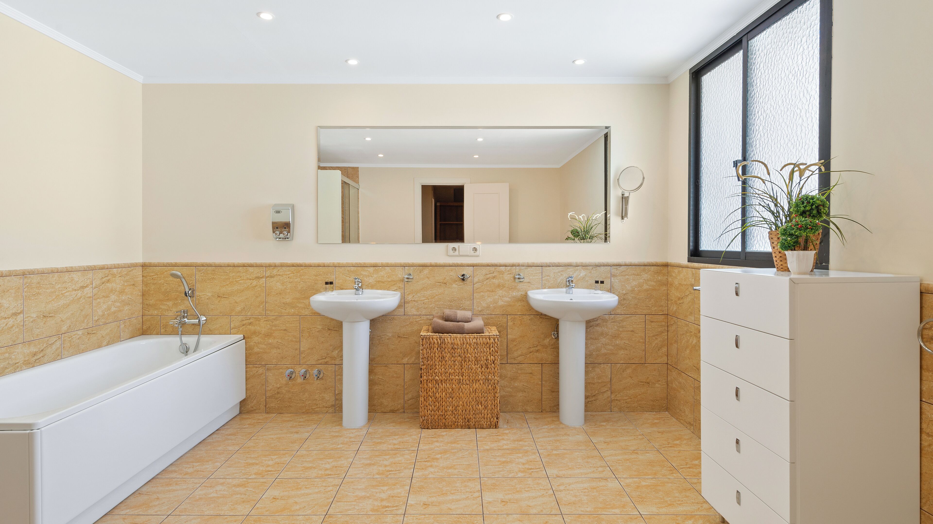 A modern bathroom with two sinks, a bathtub, and a large mirror.