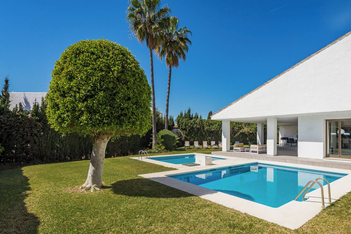 A modern house with a swimming pool, a covered patio, and a well-maintained lawn.