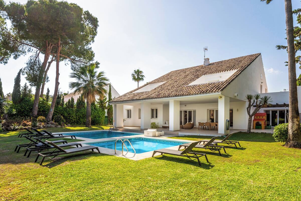 A house with a swimming pool, surrounded by a well-maintained lawn and trees.