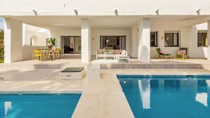 A pool area with a sunlit patio, outdoor seating, and a clear view of the pool.