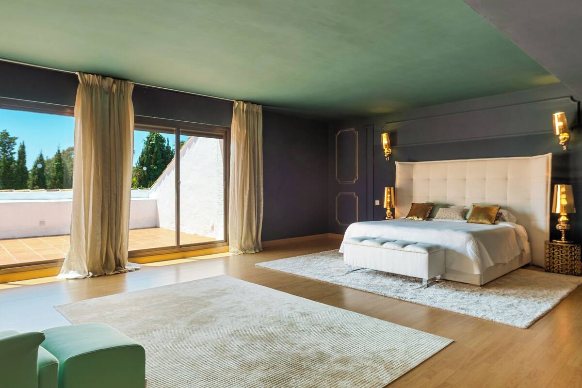 A modern bedroom with a large bed, a view of the outdoors, and a large window with curtains.