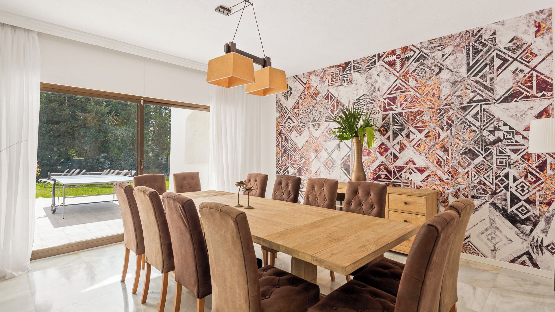 Een eetkamer met een houten tafel, bruine fauteuils en een wand met een geometrisch patroon.