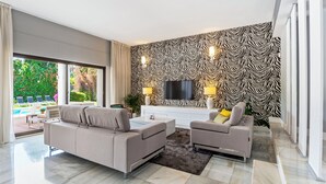 A modern living room with a sofa, armchair, and a flat-screen TV mounted on a zebra-patterned wall.