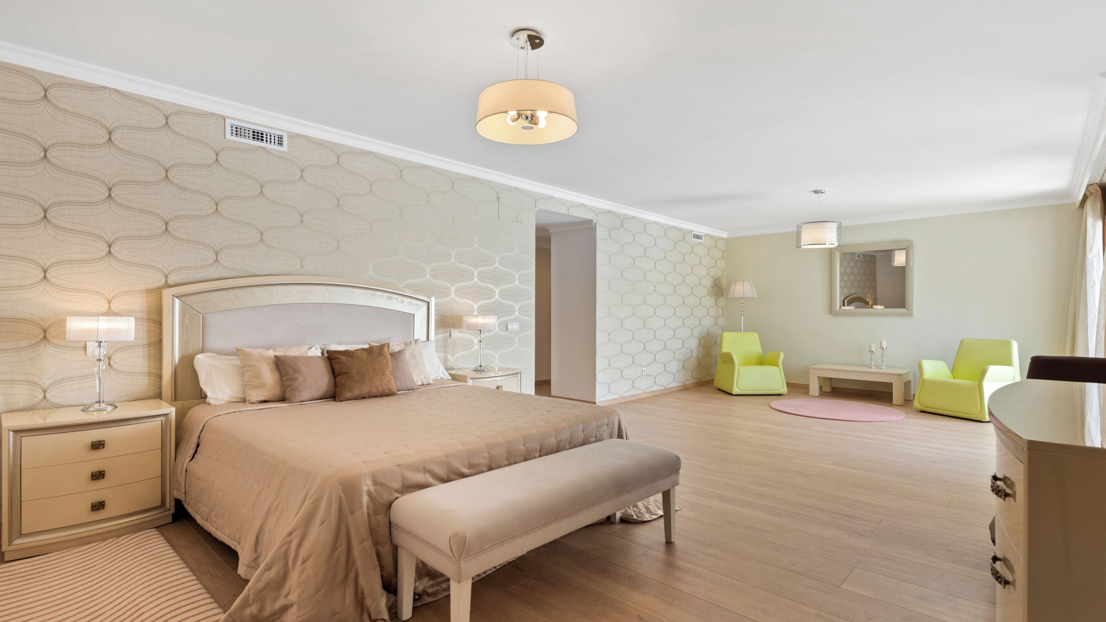Un dormitorio moderno con una cama grande, mesitas de noche, un banco, un escritorio y dos sillas.