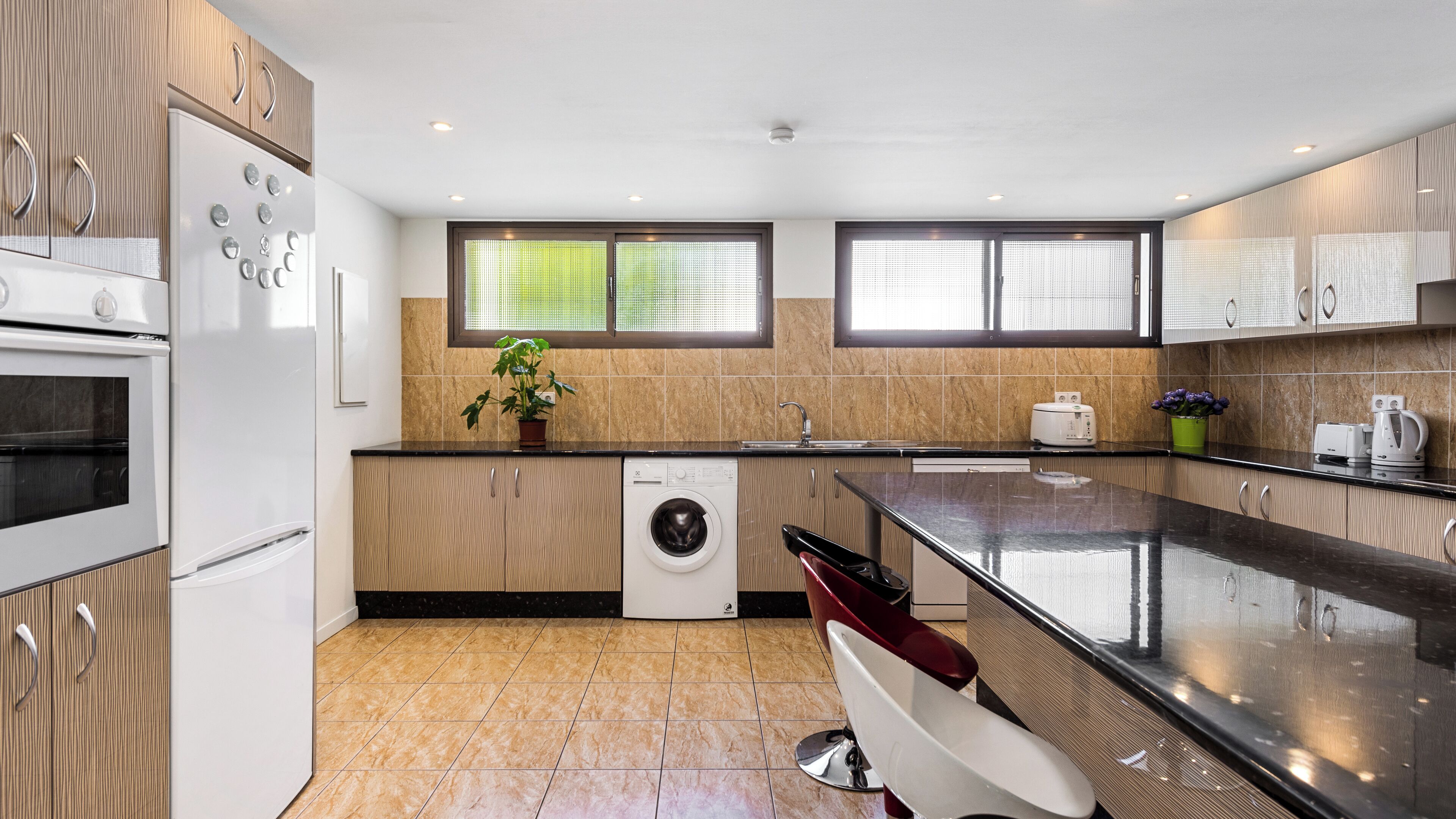 Une cuisine moderne avec des meubles en bois, un four encastré, un lave-linge et un grand îlot central doté d’un évier.
