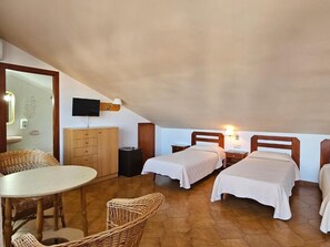 A small, cozy room with two single beds, a wooden cabinet, a television, and a dining table with wicker chairs. - Hotel Blue Spot (Malgrat de Mar)