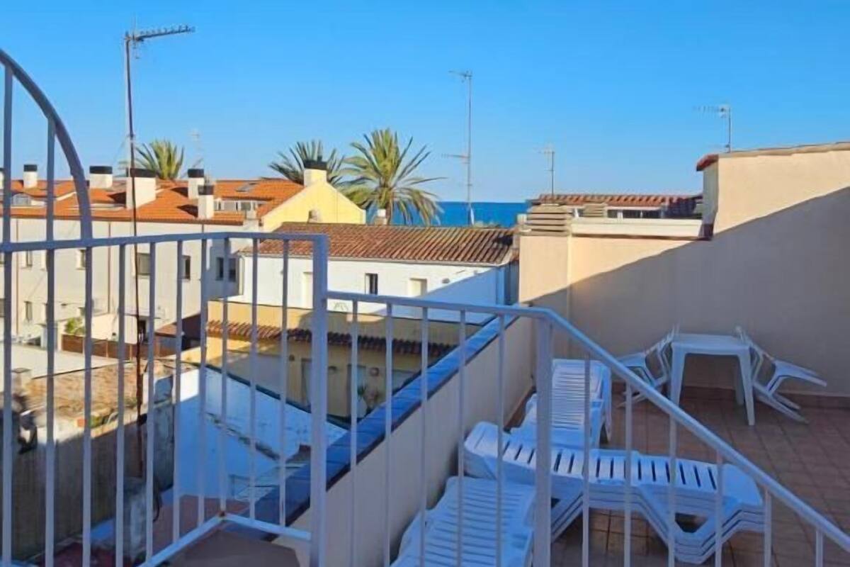Terraza en la azotea con sillas blancas y barandilla, con vistas a un barrio residencial con casas y un cielo azul despejado.