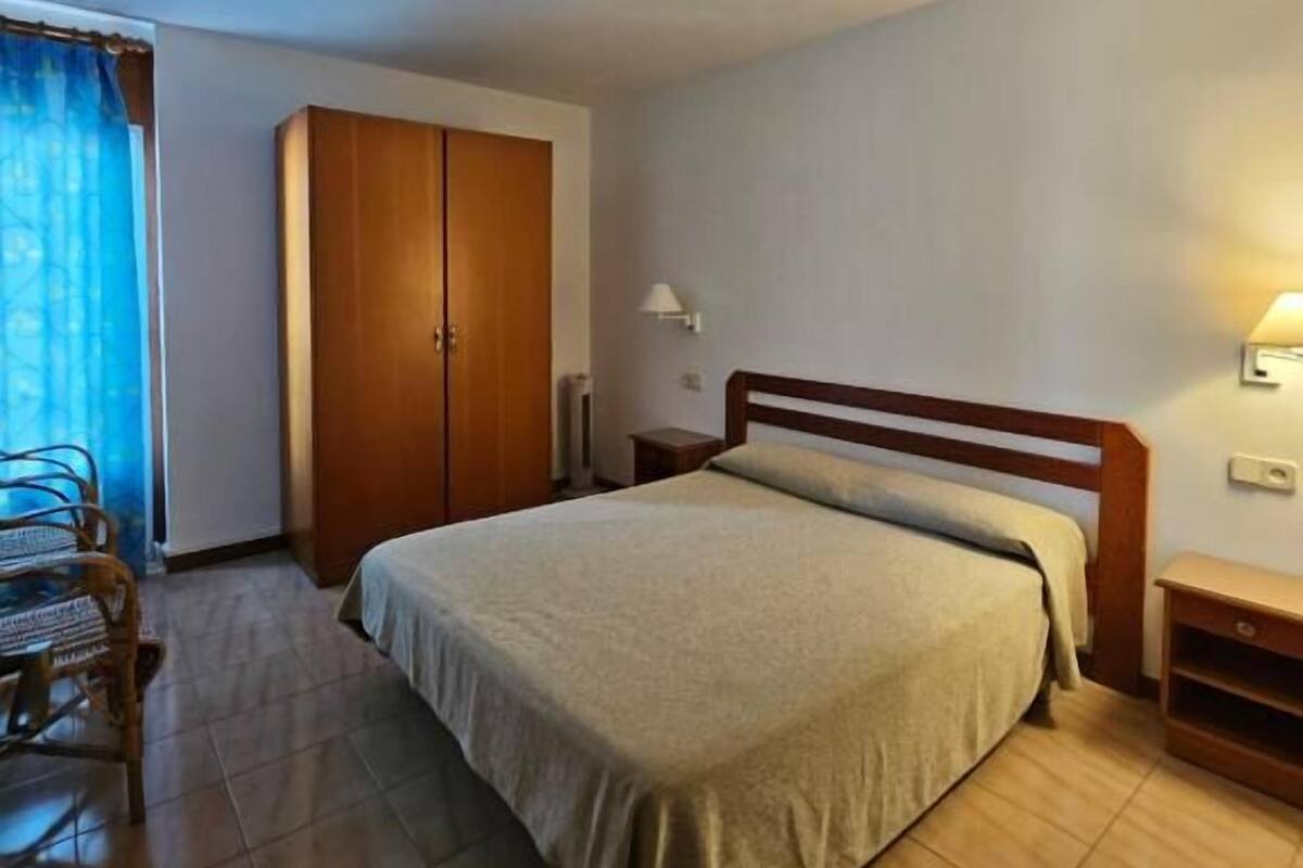Un dormitorio con cama, armario de madera y una silla.