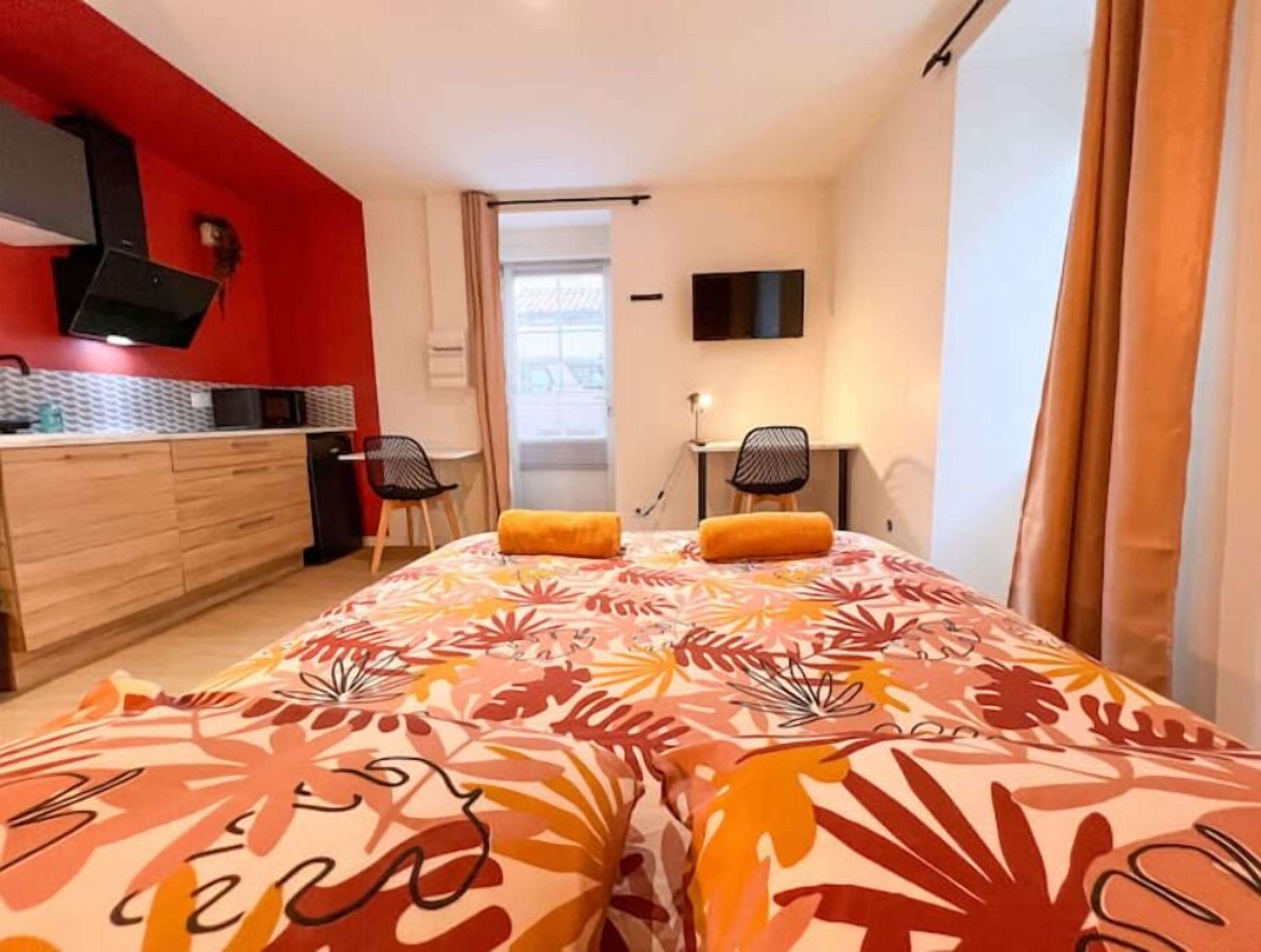 Une chambre d’hôtel de taille réduite, comprenant un lit, un bureau, une chaise et une kitchenette.