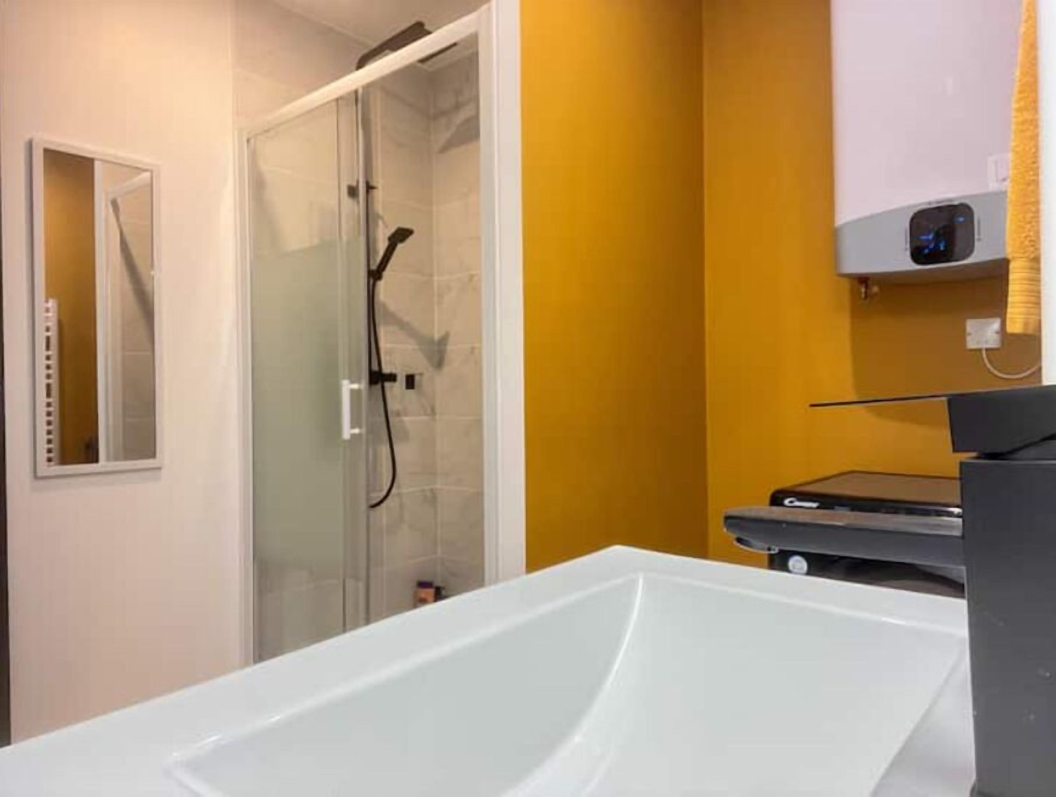 A bathroom with a white bathtub, a glass shower enclosure, and a yellow wall.