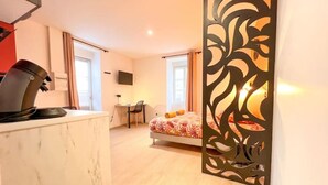 Ett modernt hotellrum med en bänkskiva i marmor, en säng med ett blommigt överkast, ett skrivbord med en stol och en dekorativ avskärmning.