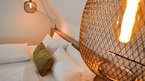 Una cama bien hecha con sábanas blancas y una almohada verde, un cabecero de madera y un colgante de luz con un brillo cálido.